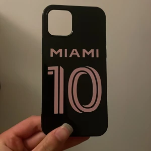 Svart mobilskal med rosa MIAMI-tryck IPhone 12 - Snyggt svart mobilskal med rosa 'MIAMI' tryck och siffran 10 på baksidan som ska föreställa siffran på Lionel Messis . Tröja. Skalets yta är blank och har ett modernt, sportigt uttryck. Passar perfekt för dig som vill sticka ut med en cool och stilren look.