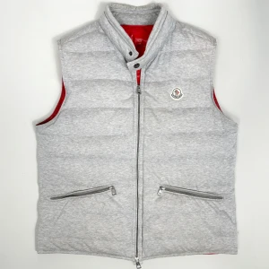 Moncler Gerard Gilet Väst - Stilren Moncler väst i modellen Gerard Gilet med röd insida. Storlek 4 sitter L/M. Skick: 8/10. Retail: 9,300 SEK. 