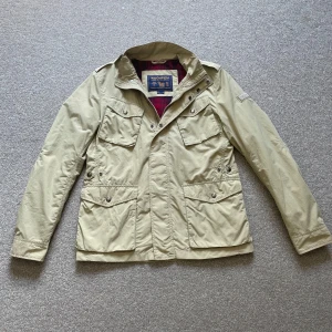 Woolrich fieldjacka beige - Säljer denna otroligt fina fieldjacka igen woolrich i storlek medium men passar även small. Den är i jättefint skick men någon enstaka bokstav på loggan har åkt av och en lite repa som syns på bilden men annars jättebra skick. Pris kan diskuteras vid snabb affär.
