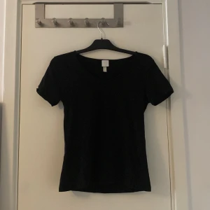 Svart t-shirt med v-ringning - En enkel svart t-shirt med v-ringad hals och korta ärmar. Perfekt basplagg som funkar till allt och är lätt att matcha med andra kläder. Skön passform och mjukt material.