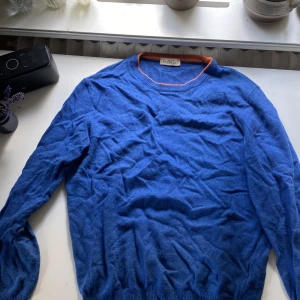 Blå tröja Paolo Ottaviani - Blå långärmad tröja från Paolo Ottaviani med rund halsringning och orange ribbad kant. Tröjan är stickad och har en klassisk passform som funkar till många olika stilar. Perfekt för dig som gillar färg och vill ha något som sticker ut lite.