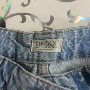 Ljusblå jeans från Lindex, storlek 40 - Ljusblå jeans från Lindex i klassisk modell med raka ben och normal passform. Jeansen har dragkedja och knapp framtill samt bälteshällor. Perfekta för en chill och avslappnad stil. Materialet är tåligt denim i bomull.