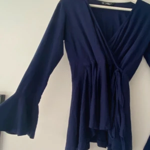 Mörkblå omlottopp med volangärm - Supersnygg mörkblå omlottopp med långa volangärmar. Toppens omlottmodell ger en v-ringad look och det flowiga tyget gör den extra skön att bära. Passar xs/S