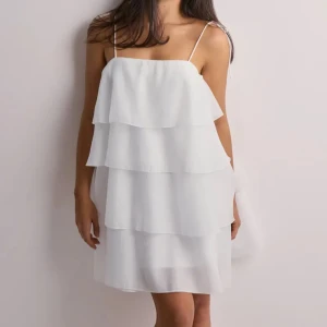 Vit volangklänning  - Superfin vit kortklänning med flera lager volanger och tunna axelband som knyts på axlarna. Inga tecken på användning, perfekt till studenten!!