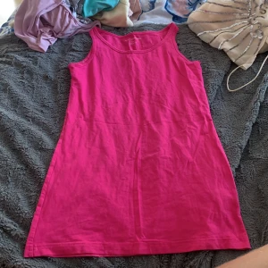 Rosa ärmlös klänning från KappAhl - En enkel och snygg rosa kortklänning från KappAhl. Klänningen är ärmlös med rund halsringning och rak passform. Perfekt för varma dagar och lätt att styla med accessoarer. Tillverkad i mjuk bomull för en bekväm känsla.