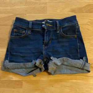 Levi's jeansshorts med upprullad kant - Mörkblå jeansshorts från Levi's, modell 710 Super Skinny. Klassisk femficksdesign med upprullad och fransig kant nertill. Snygga kontrastsömmar och midwaist passform. Perfekta för sommardagar och enkel att matcha med allt.