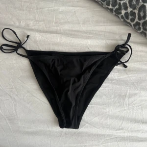 Svarta bikiniunderdelar med knyt - Snygga svarta bikiniunderdelar med knyt i sidorna. Klassisk trekantsmodell som är enkel att justera för perfekt passform. Perfekt för stranden eller poolen och lätt att matcha med olika överdelar.