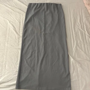 Grå långkjol med slits baktill  - Säljer en stilren grå långkjol i mjukt material. Kjolen har en rak passform och en snygg slits baktill som ger extra edge. Perfekt att styla med sneakers eller boots för en clean look.