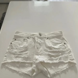 Vita jeansshorts med slitningar - Snygga vita jeansshorts med fransig kant och slitna detaljer framtill. Klassisk femficksmodell med knapp och dragkedja. Perfekta för varma dagar och en avslappnad stil. Bikbok XS 34