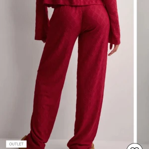 Röda vida byxor med snörning - Snygga röda byxor med avslappnad passform och vida ben. Byxorna har diskret mönster i tyget och dragsko i midjan för extra komfort. Perfekta för en chill och trendig look.