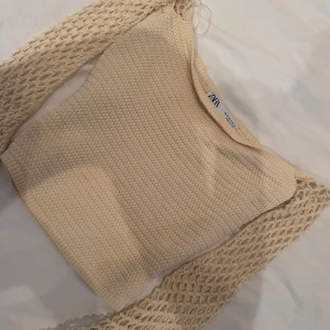 Beige stickad topp från Zara - Superfin beige stickad topp från Zara med unika virkade ärmar och croppad passform. Toppen har en snygg strukturstickad kropp och långa, luftiga ärmar med hålmönster som ger en cool och trendig look. Perfekt att styla med jeans eller kjol.