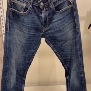 Blå Replay jeans med klassisk tvätt - Säljer ett par snygga blå jeans från Replay med klassisk tvätt och coola kontrastsömmar. Jeansen har fem fickor och en ikonisk bakficka med broderad detalj. Perfekta för dig som gillar en tidlös och avslappnad look.