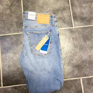 Slim Glenn ljusblå jeans Jack & Jones - Slim Glenn jeans från Jack & Jones i en snygg ljusblå tvätt. Klassisk femficksmodell med smal passform och normal midja. Tillverkade i mjukt denimtyg som ger en skön känsla och stilren look. Perfekta för dig som gillar en clean och modern vibe.