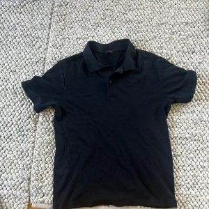 Mörkblå pikétröja från massimo dutti  - Klassisk svart pikétröja med krage och knappar framtill. Tröjan har korta ärmar och är tillverkad i mjuk bomull, perfekt för en clean och enkel stil. Passar lika bra till jeans som till shorts.