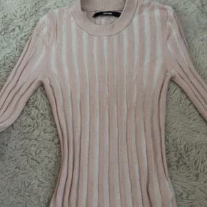 Randig rosa stickad tröja Bik Bok - Supersöt stickad tröja från Bik Bok i ljusrosa och vitt med vertikala ränder. Tröjan har lång ärm, rund halsringning och en slim passform som sitter snyggt på kroppen. Perfekt för dig som gillar en feminin och trendig look.