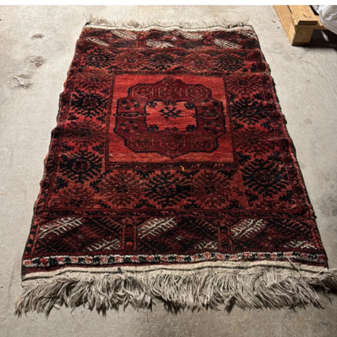 Här är ett förslag på en passande titel för bilden:“Antik röd persisk matta med geometriskt mönster och fransar”Vill du ha en kortare eller mer poetisk titel, eller kanske något mer beskrivande om skick/slitage?