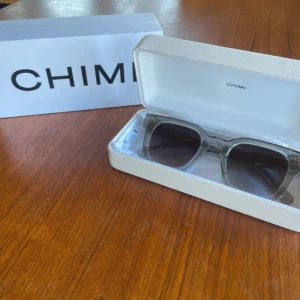 Grå transparenta solglasögon CHIMI - Snygga solglasögon från CHIMI i modell 04 med transparent grå båge och mörka glas. Rektangulär form och stilren design, perfekt för dig som vill ha en clean och modern look. Kommer med originaletui och box. Designade i Stockholm.