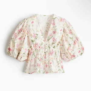 Blommig blus med puffärm - Supersöt blommig blus i vitt med rosa och gröna detaljer. Blusen har v-ringning, smockad midja och stora puffärmar som ger en romantisk vibe. Perfekt för vår och sommar när du vill känna dig extra fin.