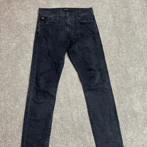 Svarta jeansbyxor från C.A.P. Studio - Säljer ett par svarta jeansbyxor från C.A.P. Studio med klassisk femficksdesign och rak passform. Byxorna har knapp och dragkedja framtill samt läderpatch med logga bak i midjan. Perfekta till vardags för en stilren look.