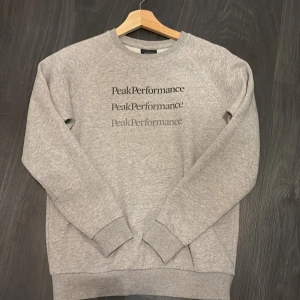 Grå sweatshirt från Peak Performance - Säljer en stilren grå sweatshirt från Peak Performance med tryck i olika nyanser framtill. Tröjan har rund halsringning och långa ärmar med ribbade muddar. Knappt använd och den ser ut som om den vore ny 