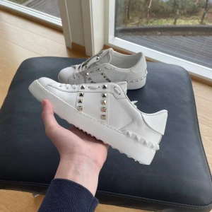  Valentino  Rockstud - Säljer ett par vita sneakers från Valentino med silvriga nitar längs sidorna och bak. Skorna har en chunky vit sula och är tillverkade i skinn. Perfekta för dig som vill ha en stilren men edgy look.
