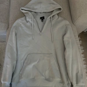 Ljusgrå hoodie från H&M - Säljer en ljusgrå hoodie från H&M med relaxed fit. Tröjan har huva med dragsko, halv dragkedja framtill och en stor magficka. Perfekt för en avslappnad stil.