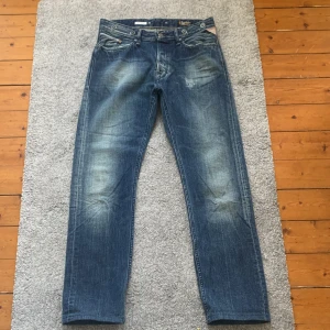 Replay jeans blåa - Säljer ett par klassiska blå jeans från Replay med raka ben och snygga slitningar. Byxorna har fem fickor, dragkedja och läderpatch med Replay-logga bak. Perfekta för dig som gillar en tidlös jeansstil.
