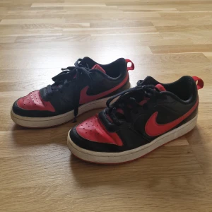 Nike sneakers svart och röd - Säljer ett par klassiska Nike sneakers i svart och rött med vit sula. Skorna har snörning och den ikoniska Nike-loggan på sidan och baksidan. Perfekta för dig som gillar sportig stil och vill ha ett par snygga och bekväma skor till vardagen.