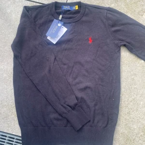 Svart tröja från Ralph Lauren - Säljer en stilren svart tröja från Ralph Lauren med det klassiska röda logotypbroderiet på bröstet. Tröjan har långa ärmar och en rund halsringning. Perfekt för en snygg och avslappnad look.
