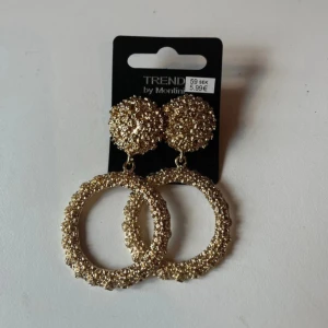 Guldiga örhängen från Montini - Säljer ett par stora, runda örhängen i guld från Montini. Örhängena har en glittrig och texturerad yta både på den runda delen och på knoppen. Perfekta för att lyfta din outfit! Helt oanvända och nya med prislapp 