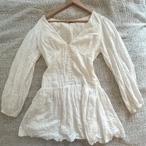 Vit klänning med broderade detaljer - Superfin vit klänning med v-ringning och långa puffärmar. Perfekt inför student eller skolavslutning. Endast använd ett fåtal gånger. Storlek M men skulle även passa som en S. 