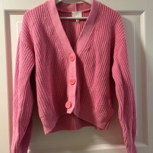 Rosa stickad kofta  - Säljer en söt rosa stickad kofta med knappar framtill. Koftan har en v-ringad design. Superfin till en sommarkväll och när som helst.