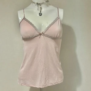 Rosa linne med spetsdetaljer - Säljer ett sött rosa linne med smala axelband och spetsdetaljer längs urringningen. Linnet har en liten rosett framtill som ger en extra touch av sötma. Materialet känns mjukt och bekvämt mot huden. Kolla gärna på mina andra annonser på samma stil 