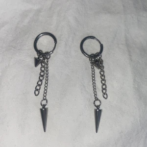 Silvriga örhängen med kedjor och konformade hängen - Säljer ett par coola silvriga örhängen med kedjor och spetsiga konformade hängen. Perfekta för dig som gillar en edgy stil och vill sticka ut lite extra. Passar både till vardagslooken och när du vill vara lite extra.