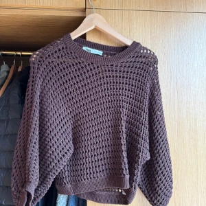 Brun stickad croppad tröja från Zara - Säljer en brun stickad tröja från Zara med grovmaskigt hålmönster. Tröjan är croppad och har långa ärmar samt ribbade muddar vid ärmslut och nederkant. Perfekt att styla över ett linne eller t-shirt.