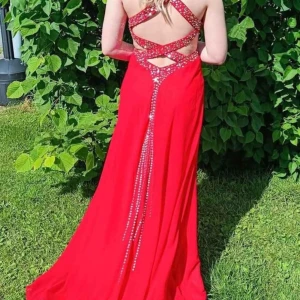 Röd långklänning med strassdetaljer - Säljer en röd långklänning med glittriga strassdetaljer och öppen rygg. Klänningen har smala axelband som korsas i ryggen och markerad midja med utskurna partier. Perfekt för bal eller festliga tillfällen.