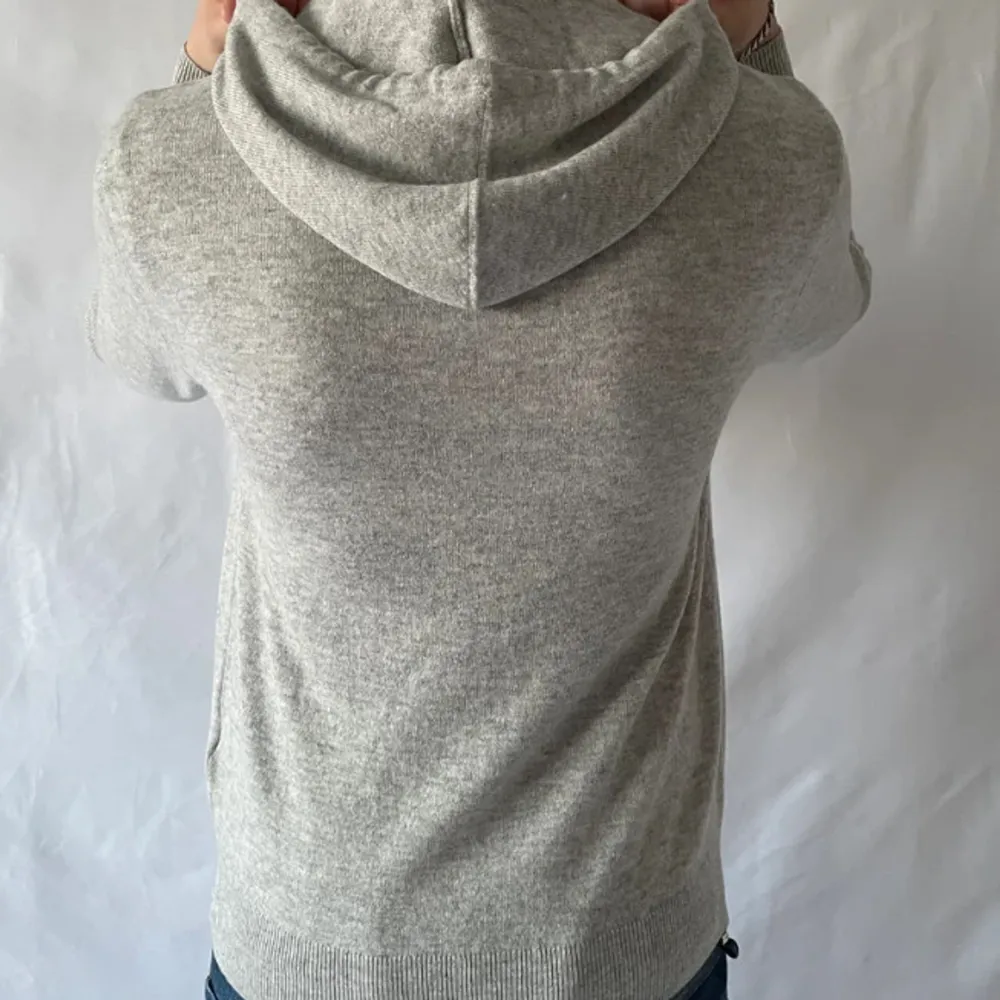 Säljer en stilren grå merino hoodie. Tröjan har en klassisk design med huva samt långa ärmar. Perfekt för en avslappnad look.. Neuletakit & Villapaidat.