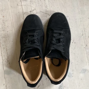 Svarta sneakers med röd sula - Snygga svarta sneakers i mocka med den ikoniska röda sulan.Skorna har snörning och en rund tå, vilket ger en klassisk och stilren look.