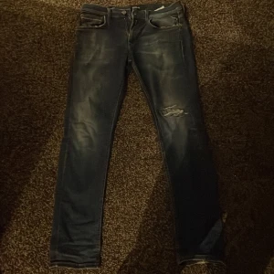 Blå jeans från Replay - Säljer ett par snygga blå replay anbass med en sliten look och klassisk femficksdesign. Jeansen har en normal passform och är perfekta för en avslappnad stil. Midjemått är W30 och längd L32.