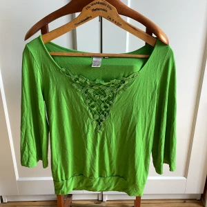 Grön topp med spetsdetalj från Filippa K - Säljer en grön topp från Filippa K i viskosblandning. Toppen har trekvartsärm och en snygg spetsdetalj framtill vid urringningen. Perfekt för dig som gillar färg och unika detaljer!