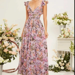 Blommig långklänning med volangdetaljer - Säljer en romantisk blommig långklänning i lila toner med volangdetaljer vid axlarna och en v-ringad fram. Klänningen har en öppen rygg med snörning som ger en elegant rygg detalj. Endast använd vid 1 tillfälle. Kostar 500kr ny. 