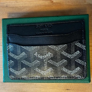 Svart korthållare - Säljer ett elegant kortfodral i svart och vitt med ikoniskt mönster. Perfekt för att hålla dina kort organiserade. Kommer i en snygg grön orginal förpackning.