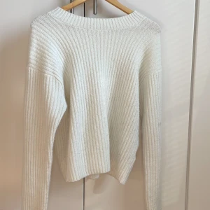 Vit ribbad stickad tröja - Säljer en vit stickad tröja med ribbat mönster. Tröjan har lång ärm och en rund halsringning. 