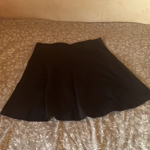 Svart kortkjol - Enkel och stilren svart kortkjol med lätt utsvängd passform. Kjolen har en slät midja och är perfekt att matcha med olika toppar för en trendig look.