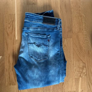 Blå Replay jeans Hyperflex - Säljer ett par blå Replay jeans med snygga slitningar och tvättade detaljer. Jeansen har klassisk femficksdesign, normal passform och raka ben. Perfekta för dig som gillar en avslappnad men trendig stil.