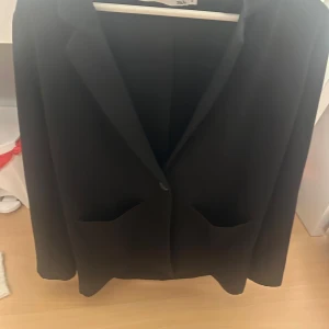 Svart kavaj från 157, storlek S - Stilren svart kavaj från 157 i storlek S. Klassisk design med två framfickor och enkelknäppning. Perfekt för dig som vill ha en tidlös och clean look. Snygg passform och enkel att matcha med olika outfits.