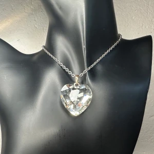 Vintagehalsband med kristallhjärta – retro Y2K-glam med wow-effekt - Statement-halsband med stort hjärthänge i slipad kristall. Ljusreflekterande och iögonfallande design med silverfärgad kedja. Troligen från tidigt 2000-tal. Kedjan är ca 48 + 6 cm, hänget ca 3,7 × 2,9 cm. Perfekt för dig som gillar dramatisk stil med romantisk twist. Auktionsfynd. Fint vintageskick.  Priset är redan lågt, så jag prutar inte – men erbjuder gärna rabatt vid köp av flera saker. 