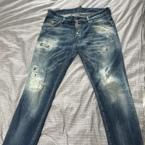 Dsquared2 slitna blå jeans herr - Riktigt snygga blå jeans från Dsquared2 med slitna detaljer och ljusa partier framtill och baktill. Klassisk femficksmodell med raka ben och coola slitningar för en edgy look. Jeansen är i bomull och har normal passform.