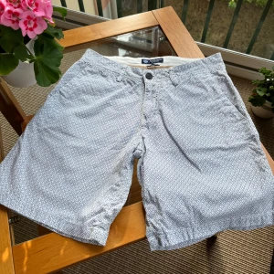 Mönstrade shorts från North Sails - Snygga vita shorts från North Sails med blått geometriskt mönster. Två fickor fram och två bak. Perfekta för sommardagar. Bomull 98% och elestan 2%. Endast använda ett par gånger.  Storlek 36. 