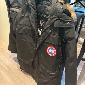 Svart dunjacka från Canada Goose - Säljer två svarta Canada Goose dunjacka med ikonisk patch på bröstet och pälskantad huva. Jackan har flera stora fickor, dragkedja och är perfekt för kalla vinterdagar.  Jackorna är i XS ( kvinna ) S ( Herr ) PS jackorna är stora i storleken. Båda jackorna är Äkta och aldrig använda, säljer jackorna då de är mina föreldras gamla och dom Aldrig riktigt föll för dom och pengarna kan gå till annat. Köp en för 1500 båda för 2500! Skriv gärna om ni undrar om mer. 
